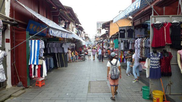 Shoppers in the city of Putian in Fujian Province walk along a narrow alleyway lined with stalls selling brightly colored clothing.