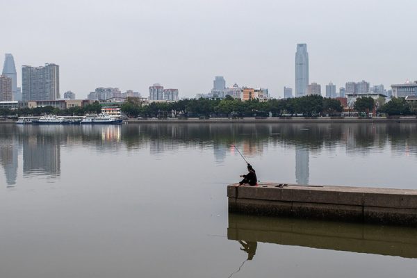Man fishing in lake against urban skyline