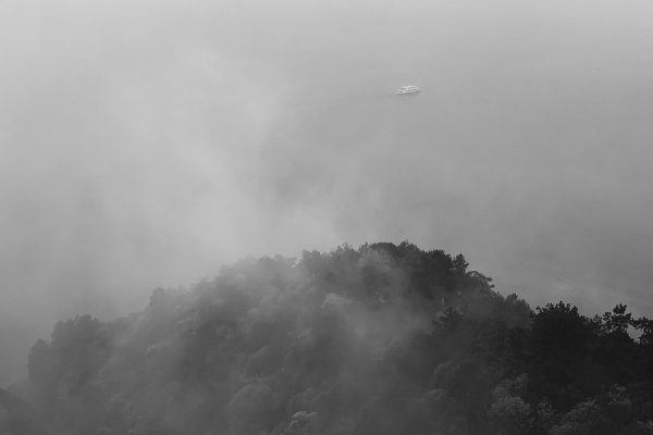 A distant boat on the lake beyond a wooded hill, viewed from above through mist