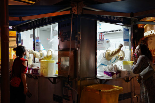 Workers at a Shanghai COVID testing booth administer tests using window-mounted isolation gloves