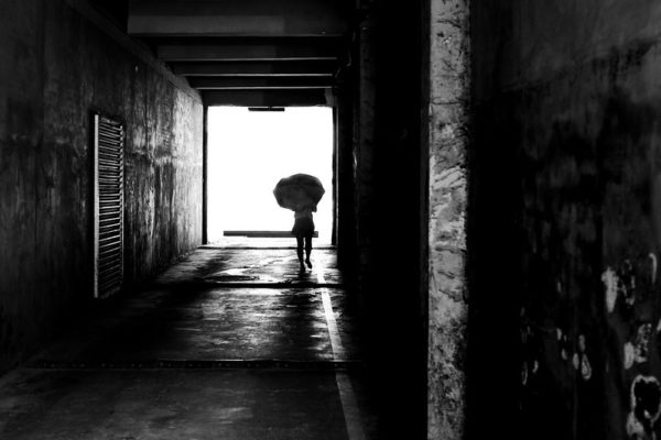 A figure with an umbrella silhouetted at the end of a dark passageway