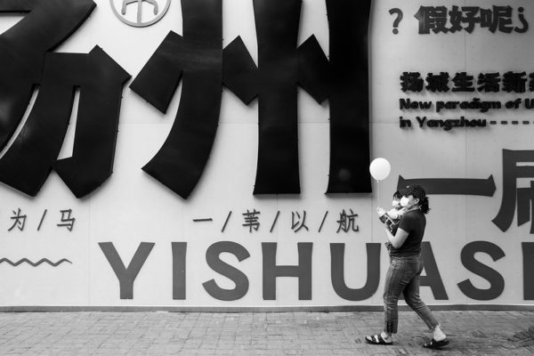 A woman holding a baby holding a balloon walks in front of a wall covered with signage