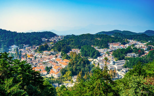 Amid heavily wooded rolling hills, there are several clusters of low white buildings with rooftops of orange or gray tile.