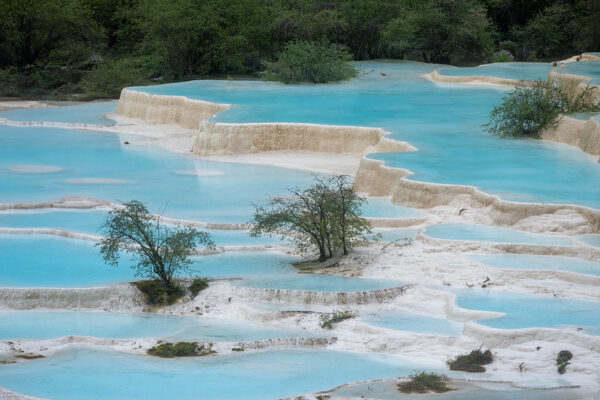 A series of calcified ponds with pale white edges and crystal clear turquoise waters seem to cascade down a hillside at the World Heritage site of Huanglong National Park in Sichuan province, China.