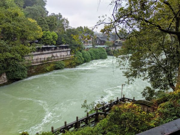 A surging river flows past the stone walls, wooden houses and lush greenery of Dujiangyan, Sichuan Province, known for its ancient irrigation system.